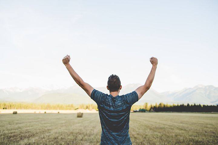 A man outdoors facing away from the camera with his arms raised, fists clenched